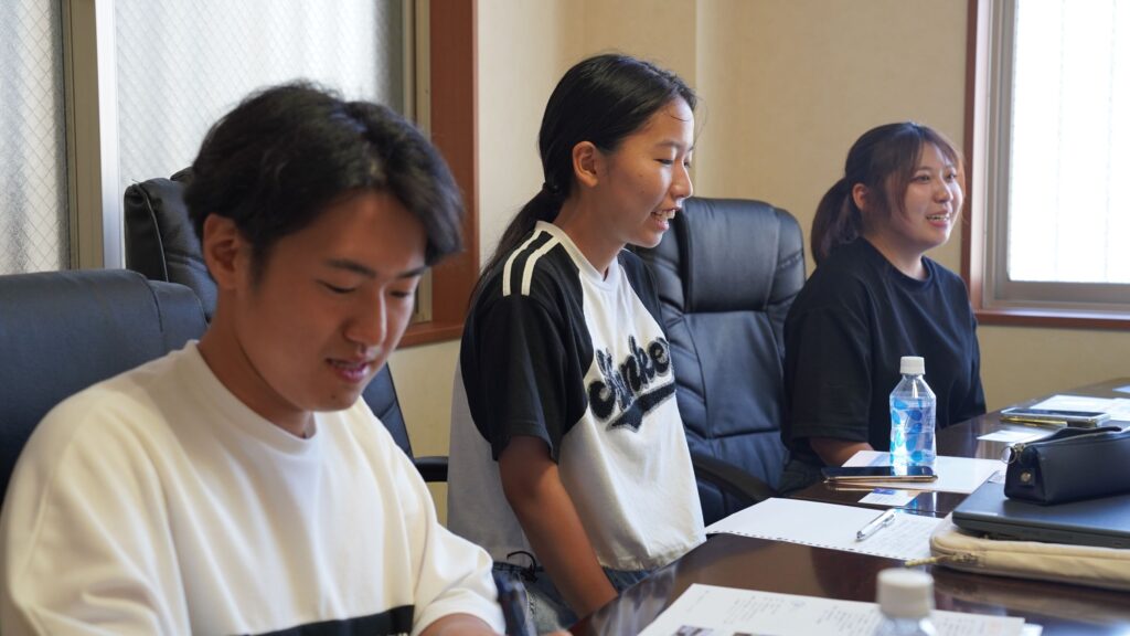 アイデアル株式会社への取材中に、自身の質問や意見を述べる学生記者(中央)。奥には別の学生、手前には別の記者が座る。